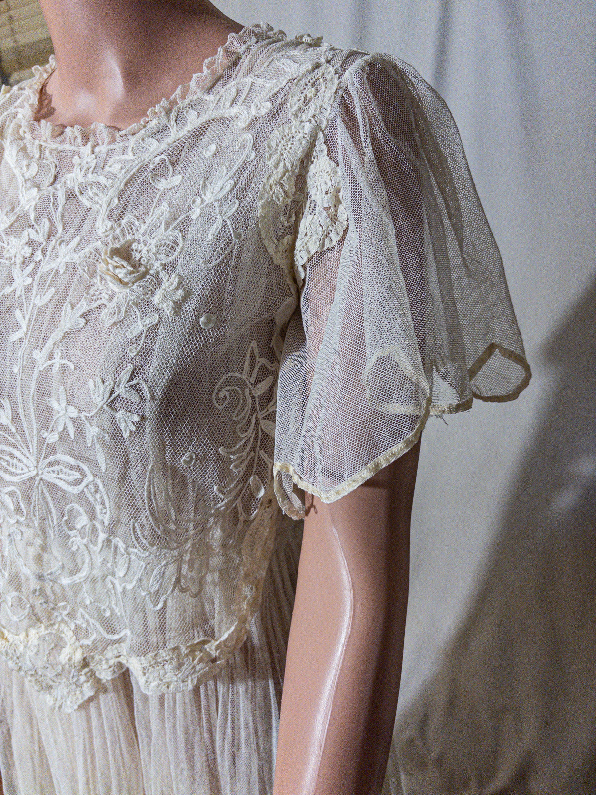 Mannequin wearing a vintage-style lace dress with sheer sleeves against a plain background